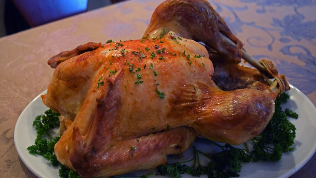 Whole golden-brown roasted turkey on a white platter, garnished with fresh parsley — Thanksgiving centerpiece